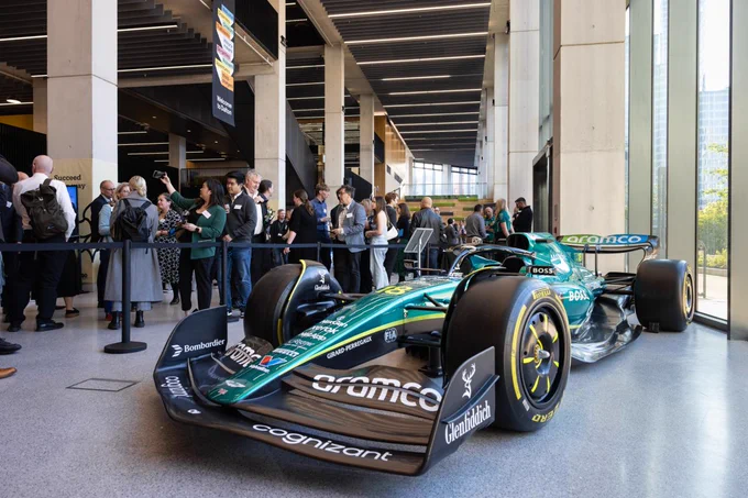 Visitors examine an Aston Martin Formula 1 race car displayed at a public indoor venue.