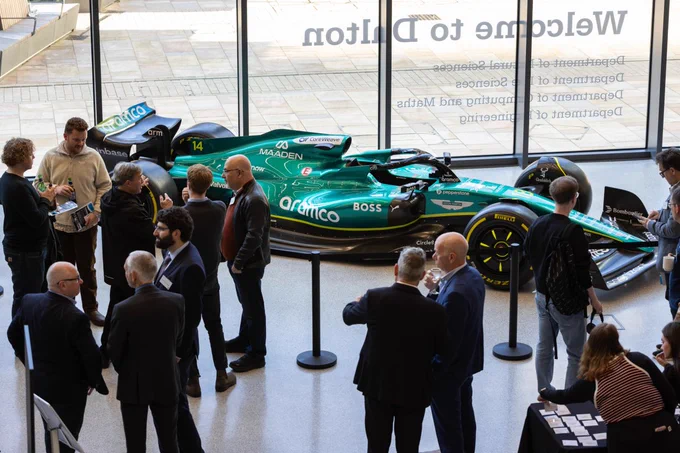 Group of individuals gathered around an Aston Martin Formula 1 race car on display at an indoor event.