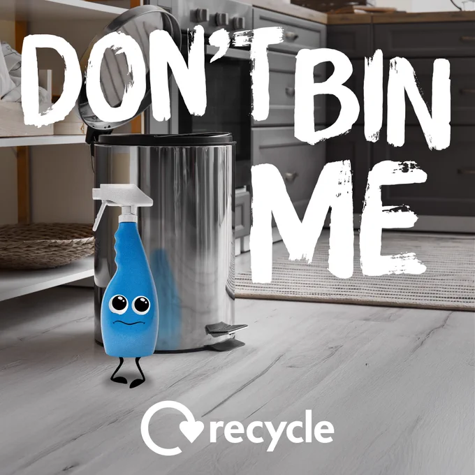A trigger spray bottle with a cartoon face standing next to a metal bin