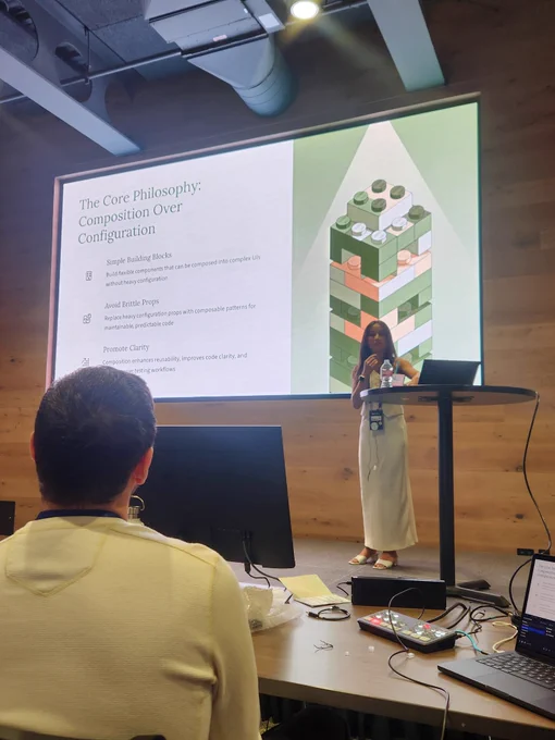 A young woman on stage at a rech conference with a screen behind her titled 'the philosophy: composition over configuration '

