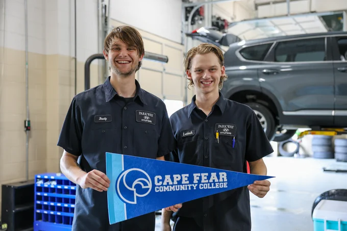 two automotive techs standing in car shop holding CFCC flag
