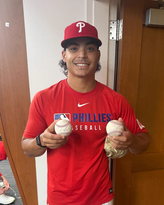 Jesús Luzardo smiles and holds two autographed baseballs in the Phillies clubhouse.