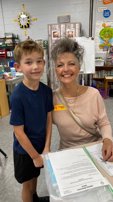 third grade boy stands next to his grandma who is sitting. they have large smiles and are looking directly at the camera. 