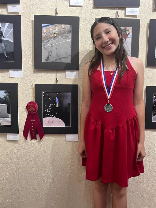 student standing next to her artwork with a ribbon and medal 