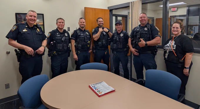 Six police officers and one civilian stand smiling around an oval conference table.