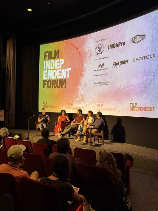 Five people on stage, sitting on chairs, engaging on conversation in front of an audience.
