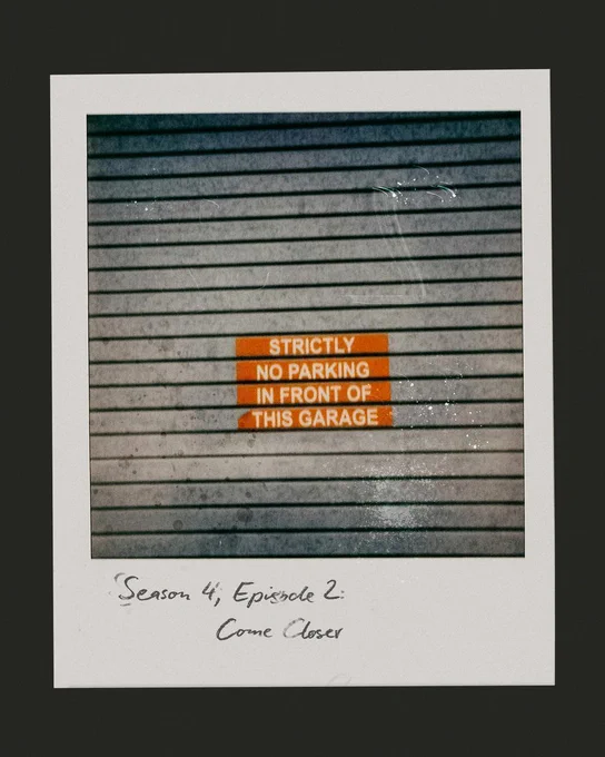 A polaroid picture of a garage door with a wet surface displays a bright orange sign reading "Strictly No Parking in Front of This Garage." Writing on the polaroid reads: "Season 4, Episode 2: Come Closer." The mood is serious and cautionary.