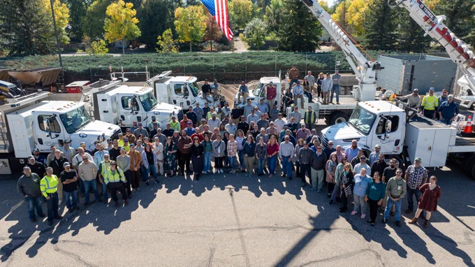 Group photo of Fort Collins Utilities Light and Power taken in 2025 in front of utility trucks and an American flag.