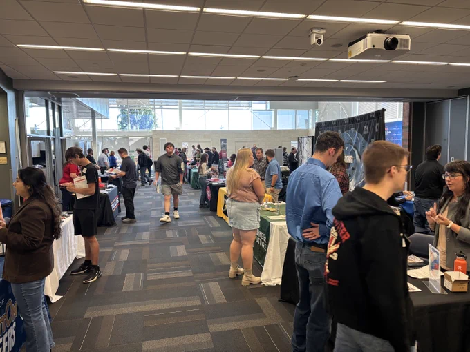 A busy career fair event in an indoor setting with various booths and attendees interacting and networking.