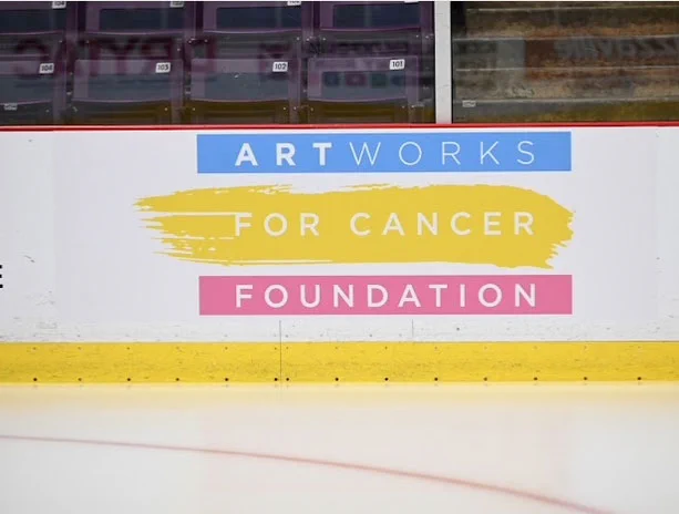 The ArtWorks for Cancer logo on the boards of the ice hockey rink at the CAA Centre in Brampton