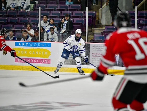 The Brampton Steelheads hockey team plays against opponents on the ice, with the ArtWorks for Cancer logo on the boards behind them