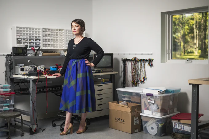 Sophia Brueckner standing in her home studio filled with electronic equipment and components, with a window showing greenery outside. 