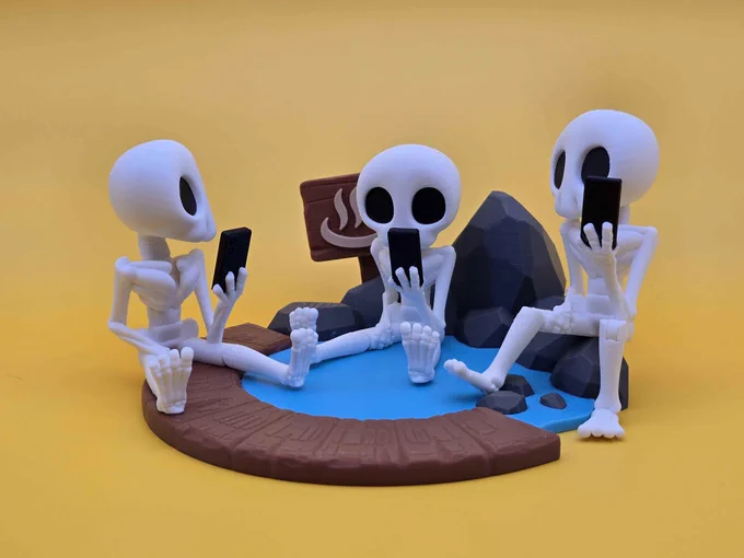 Three Skeleton Hazy figures sit around a 3D printed hot spring display with rocks, wood planks, and blue water. Each skeleton gazes at its phone, combining chill vibes with dark humor.