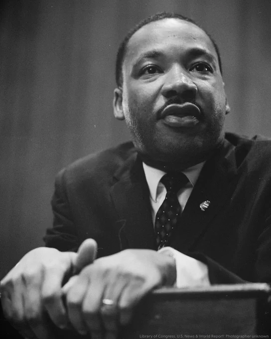 Portrait of Dr. Martin Luther King Jr. leaning over a podium while speaking.