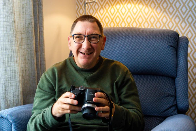 A picture of a man smiling, holding a camera.