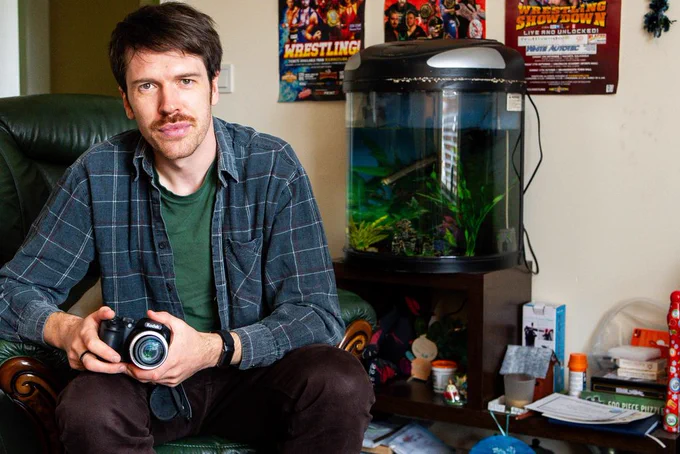 A picture of a man smiling, holding a camera.