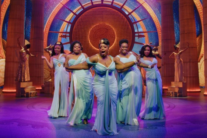 A photo showing five performers in blue grecian outfits on a warmly lit stage made to look classical 