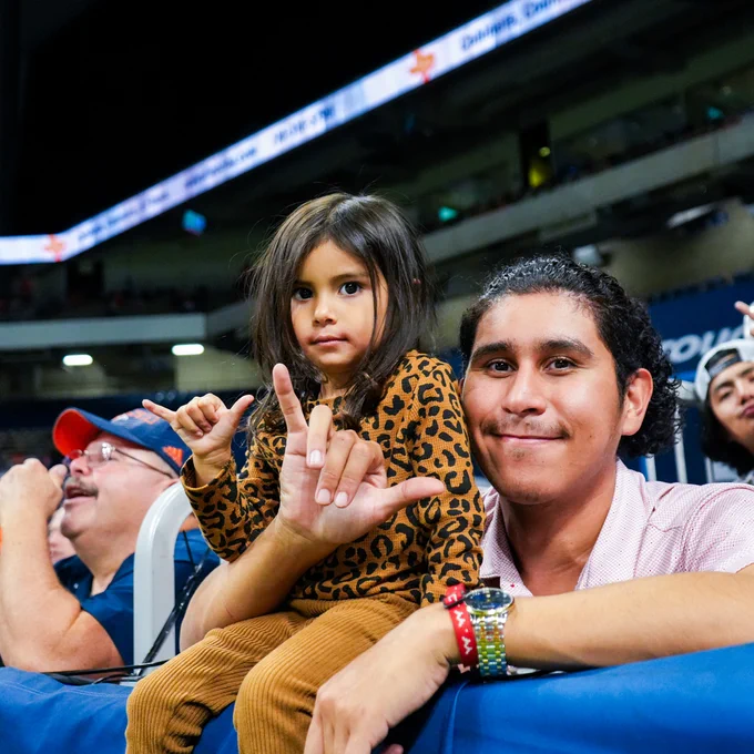 Adult and child spectator at a Homecoming football game making a 'birds up' hand gesture.