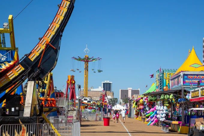 View of the lively outdoor Mississippi State fairgrounds with colorful stalls, amusement rides, and games on a bright sunny day.