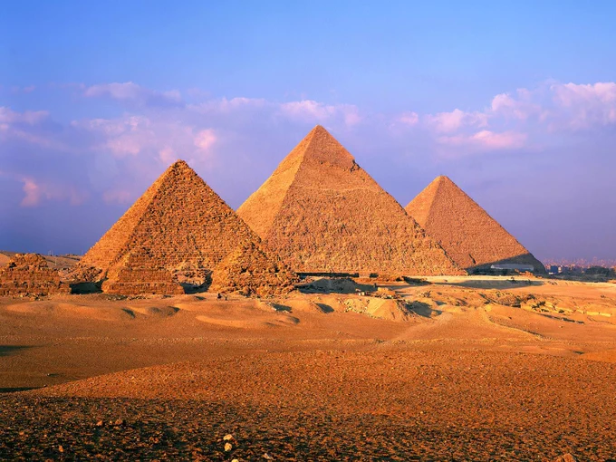 The Great Pyramids of Giza under a clear blue sky, with the desert foreground bathed in warm sunlight.