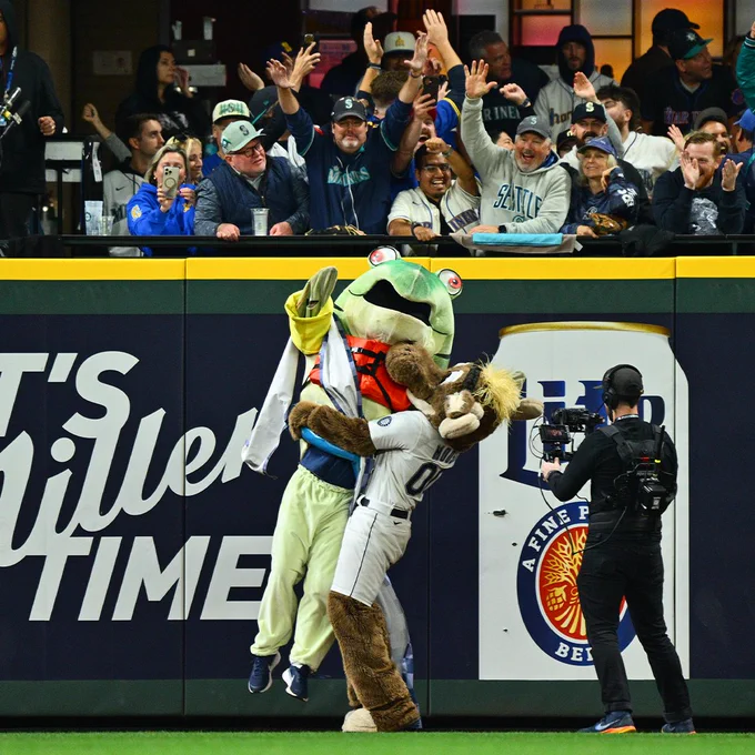 The Mariner Moose lifts Humpy the Salmon up in celebration after Humpy won the Salmon Run for the first time ever. Mariners fans can be seen going wild in the background.
