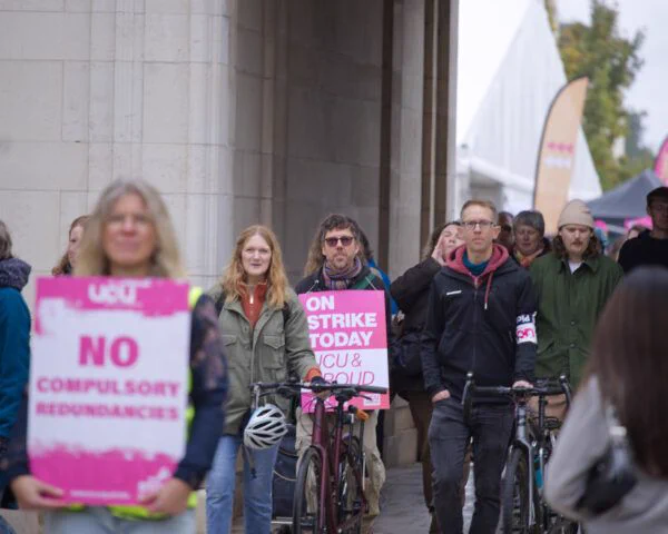 A photo of people holding picket signs and walking into Trent courtyard
