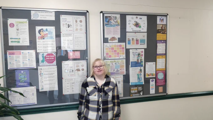 A photograph of a lady in front of two wall mounted display boards.
