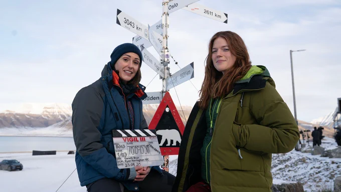 Suranne Jones and Rose Leslie stand on set in a snowy location holding a clapperboard signalling the start of shooting on Vigil series 3