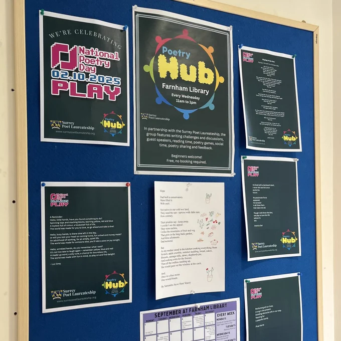 A noticeboard at Farnham Library, with out of focus poems written by the poetry hub group. At the top is a larger poster which reads 'National Poetry Day 02.10.2025' and 'Poetry Hub Farnham LIbrary' with the Surrey Poet Laureate logo.
