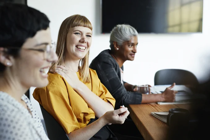 Photo of three colleagues talking and smiling during a team meeting in a bright room