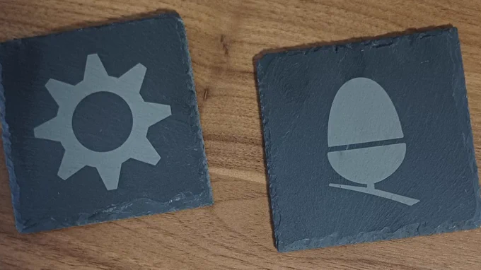 Two slate drinks coasters engraved with a RISC OS Cog logo on one and an Acorn Computers motif on the other.