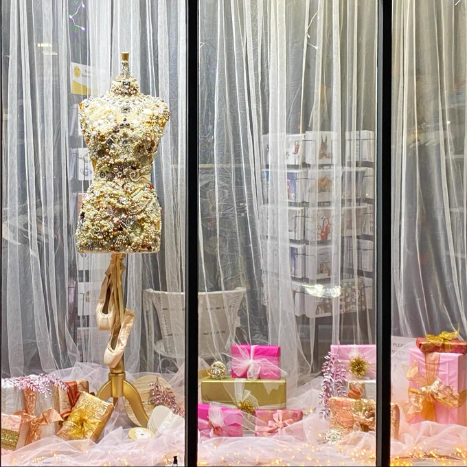This is a show window with a mannequin surrounded by wrapped presents.
