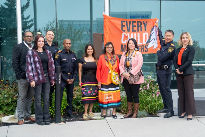 Individuals posing, with Deputy Chief of Peel Police holding up 'Every Child Matters' Flag in front of Peel Police's Headquarters