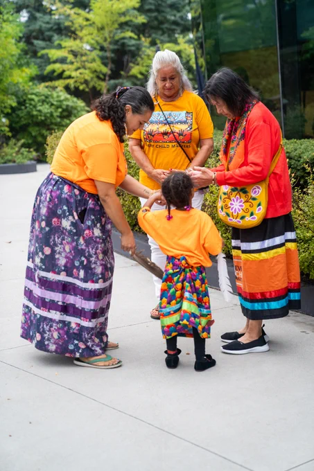 Group of individuals and child in gathered in a circle. 