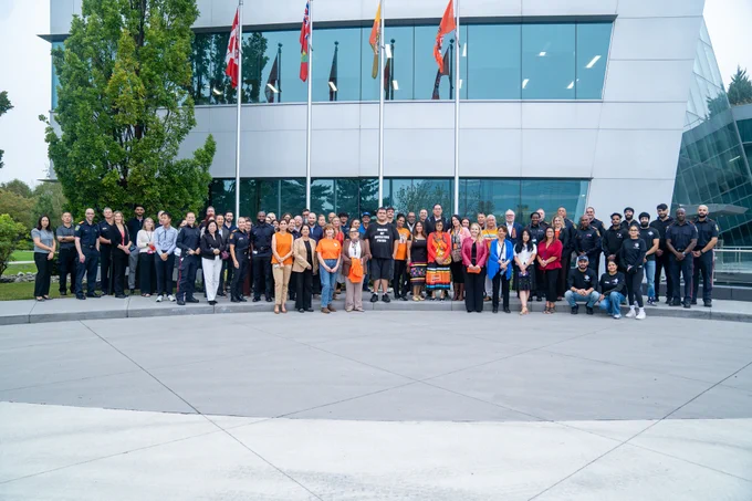 Group of individuals posing in front of multiple flags for National Day of Truth and Reconciliation and Orange Shirt Day.