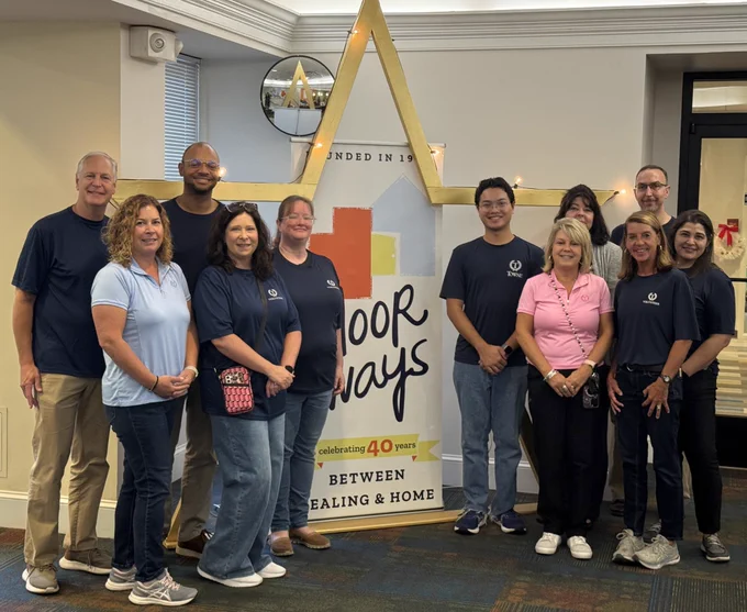 A smiling group of volunteers stands in front of The Doorways banner in the lobby of The Doorways