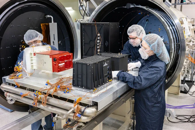 Three engineers wear hairnets, masks and gowns as they prepare sensors for the next generation of detectors to undergo thermal vacuum testing at Sandia. 