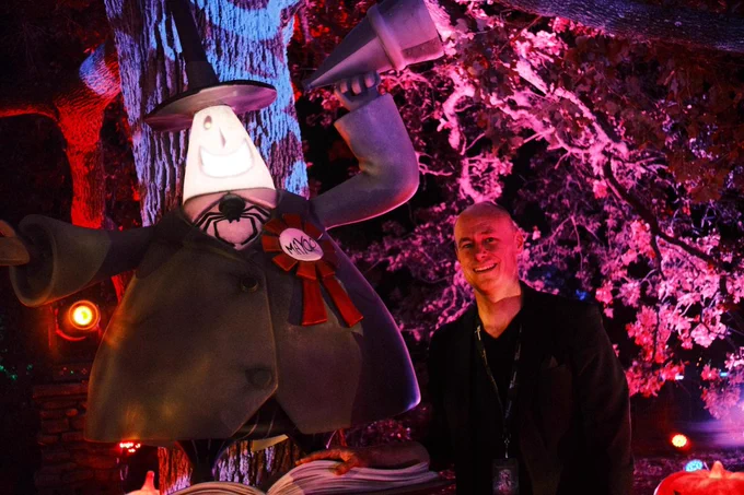 The picture shows executive and Artistic Director of Texas Performing Arts Bob Bursey standing next to The Nightmare Before Christmas character, The Mayor, at The Nightmare Before Christmas light trail located at Lady Bird Johnson Wildflower Center. The background features strong colorful lights in shades of red and violet. 
Picture by Izabella Hernandez.