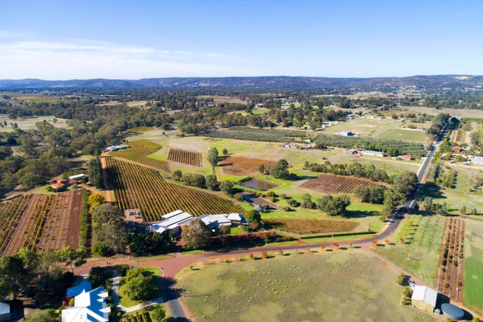 Aerial view of a rural landscape showcasing cultivated fields, vineyards, and farm buildings on a sunny day. Image promoting AgriFutures Australia's Request for Quote 'Next Generation Connectivity for Australian Agriculture: Assessing the Impact of LEOSat-Enabled Connectivity'.