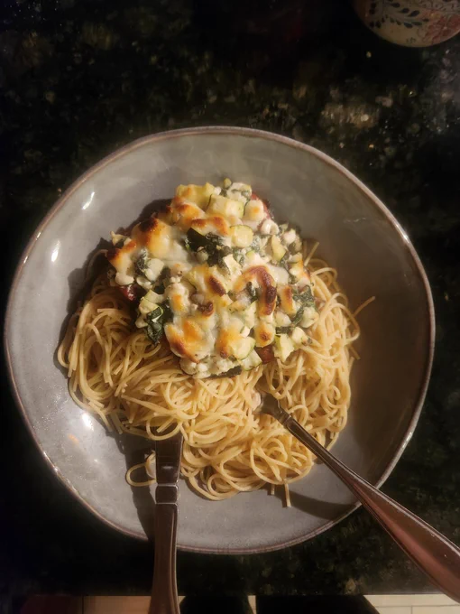 Portobello mushroom stuffed with green vegetables and topped with melted cheese that has browned, served on top of buttered angel hair pasta.