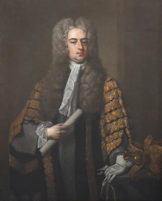 Portrait of a man stood with on hand on a table and the other held to his chest, with a scroll in his hand. He wears a long, curly grey wig. He has black robes with gold braid detail over the shoulders and sleeves, and a white lace collar and cuffs.