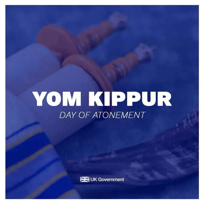 Square graphic with white text that reads YOM KIPPUR - DAY OF ATONEMENT on a blue background laid over an image showing Torah scrolls, with the UK Government logo at the bottom.