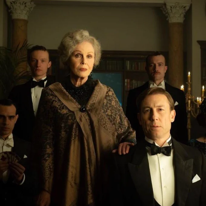 A group shot of six people dressed in old fashioned, smart clothing, as if in a party.  The men are in tuxedos.  The image is dark and eerie.