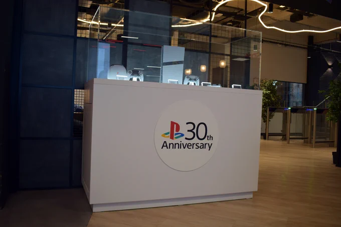 Display celebrating PlayStation's 30th Anniversary. A white podium showcases PlayStation consoles and controllers in a glass case, with the anniversary logo prominently featured.