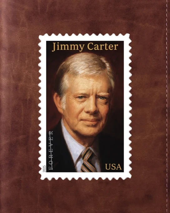 A U.S. postage stamp with a portrait of former President Jimmy Carter is shown against a textured brown background. The stamp has a white serrated edge, and Carter's name is printed in white at the top, while "FOREVER" and "2025" are printed vertically on the left side. "USA" is printed in white at the bottom right. Carter is depicted wearing a dark suit, a white collared shirt, and a striped tie, looking directly forward with a serious expression.