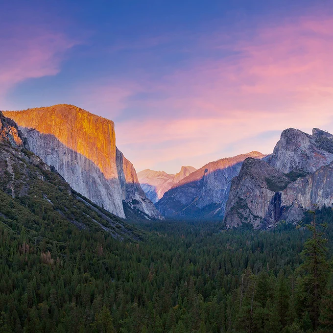 Sunset view of El Capitan and the Yosemite Valley in Yosemite National Park, with warm light on the cliff faces and a vivid blue sky.