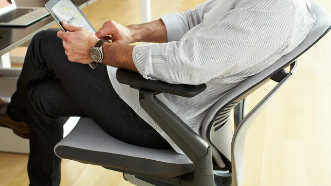 Man in a striped shirt sitting in a Gesture office chair using a tablet at a desk.