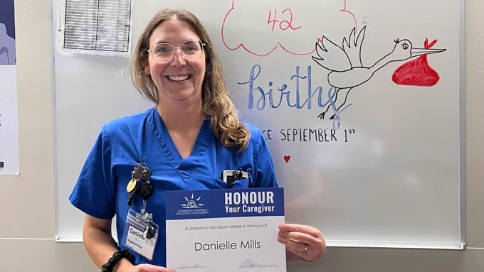Danielle Mills holding a certificate with her name in front of Labour and Delivery.