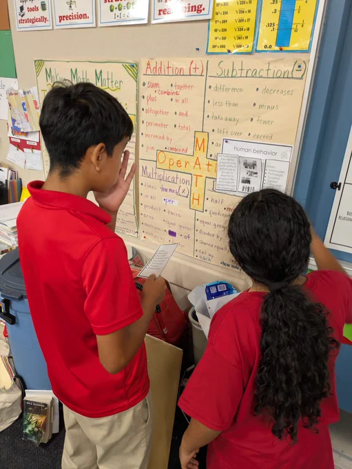 2 students dressed in red shirts and khakis read a description on human behavior.