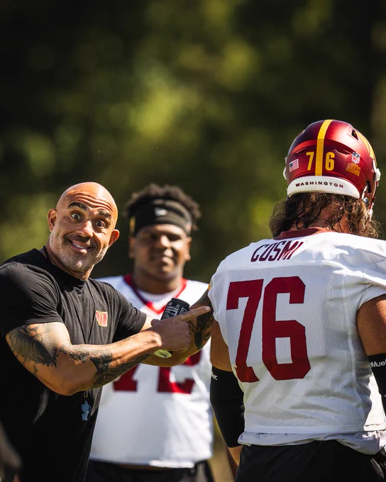 Photo of Sam Cosmi and Bobby Johnson at practice. Johnson is pointing at Cosmi and smiling. 